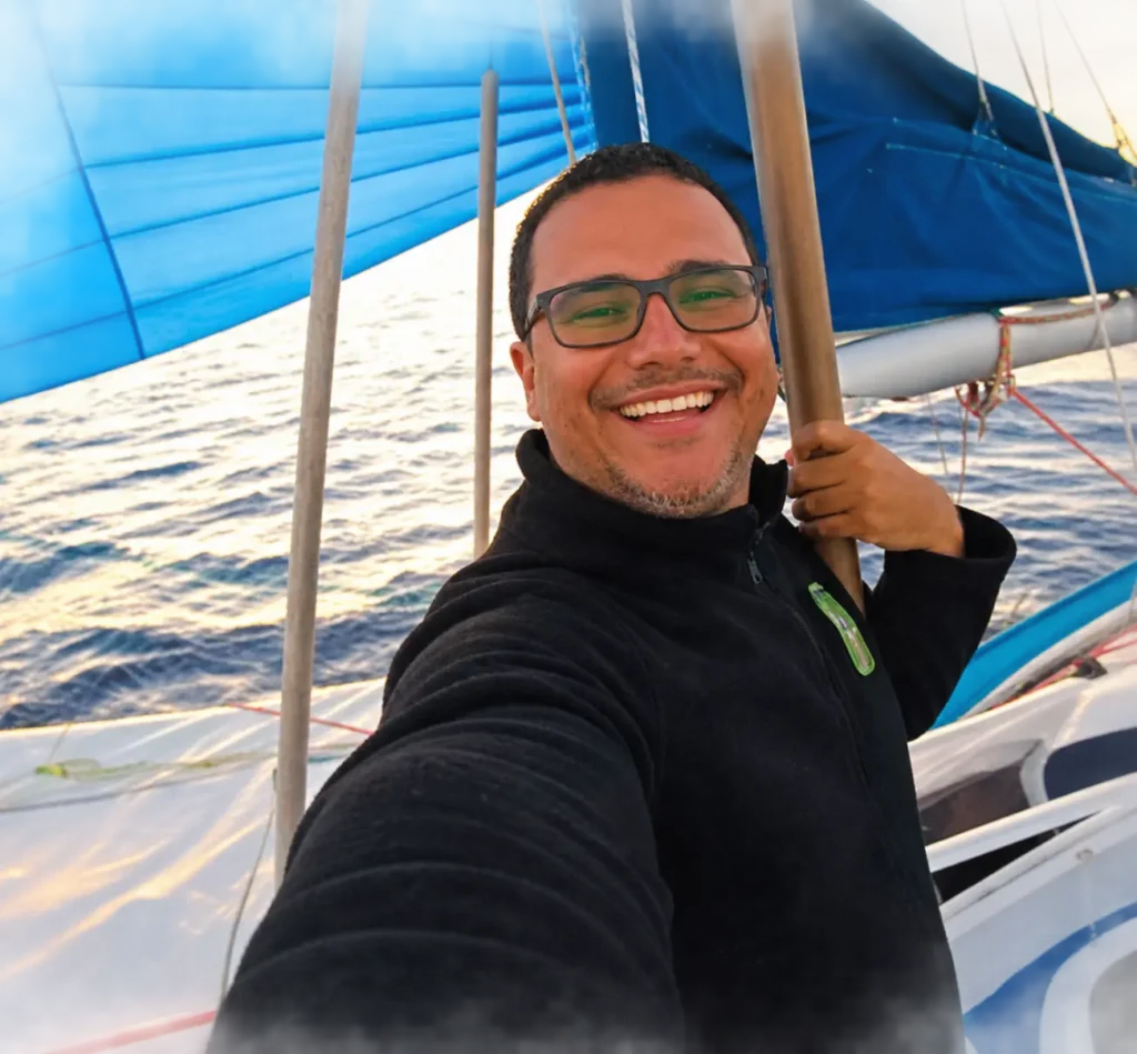 Juca Andrade a bordo de um veleiro com vela azul.